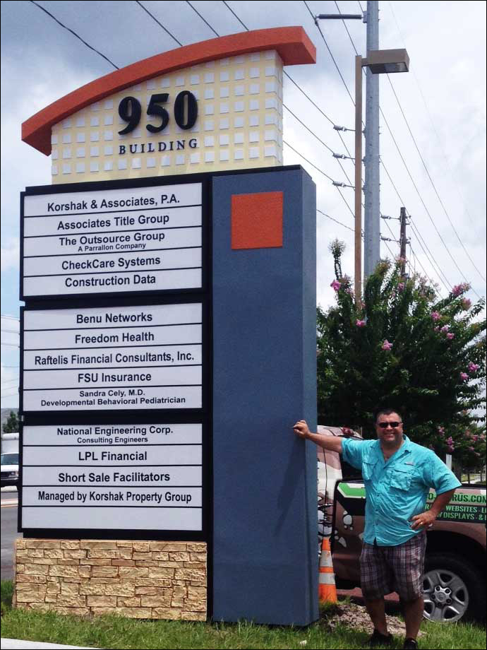 Alan Migliorato snanding next to a tall custom monument sign for the 950 building in Casselberry